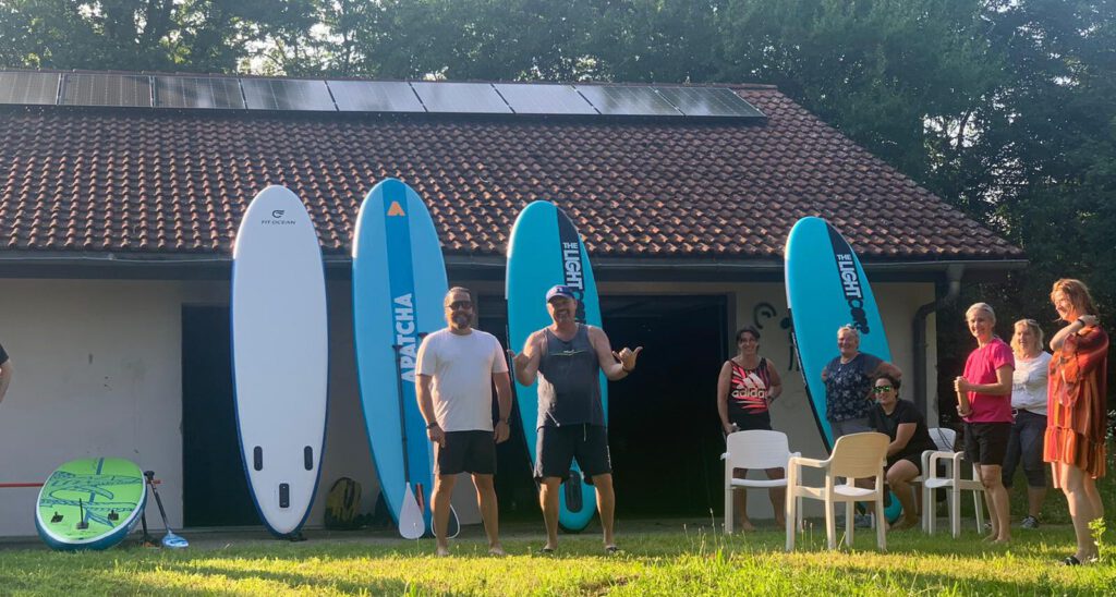 SUP-Boards an der Wand des Bootshauses, davor Kursteilnehmer